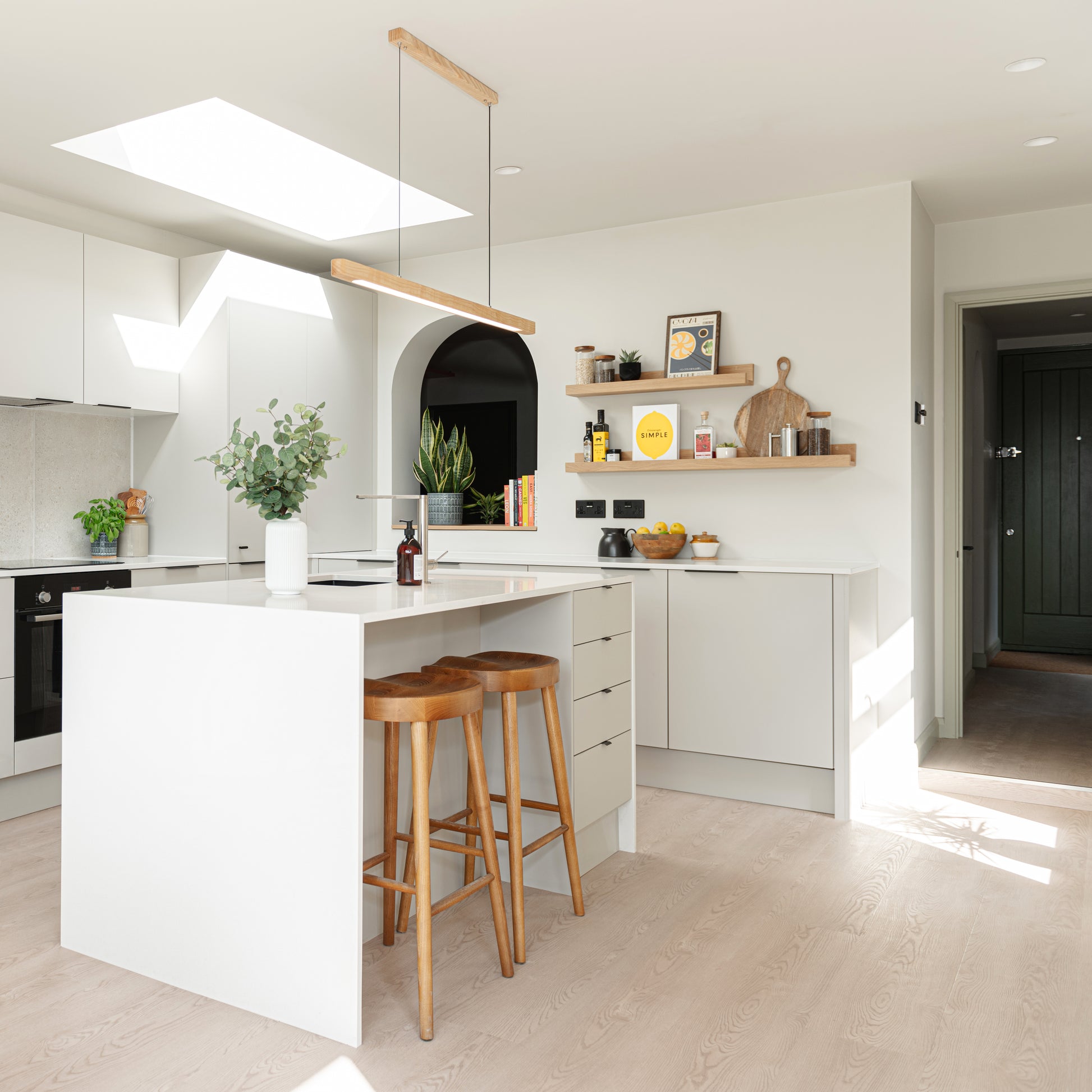 Modern kitchen with white island, wooden stools, and shelves with decor items.