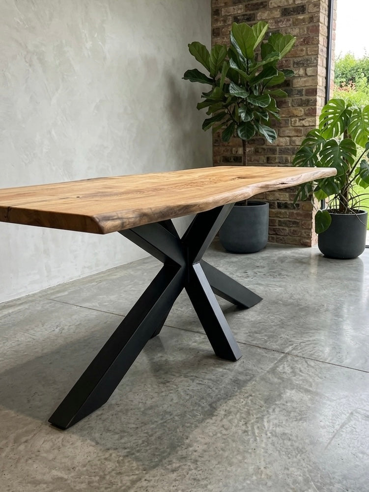 Wooden table with black metal legs in an outdoor setting with plants and a brick wall.