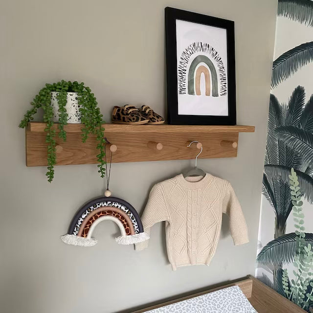 Wooden shelf with a plant, shoes, and a sweater hanging on a wall with decorative rainbow art.